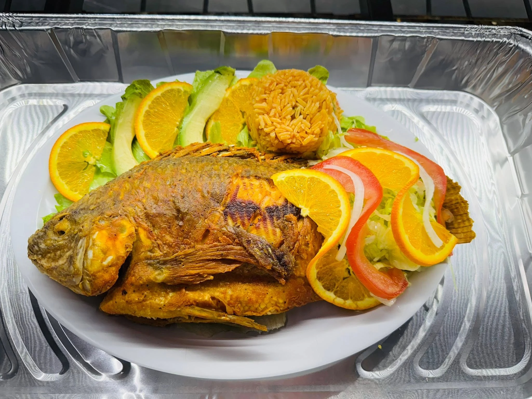 A prepared fried fish plate with rice, salad, avocado and orange slices from Carniceria Camargo