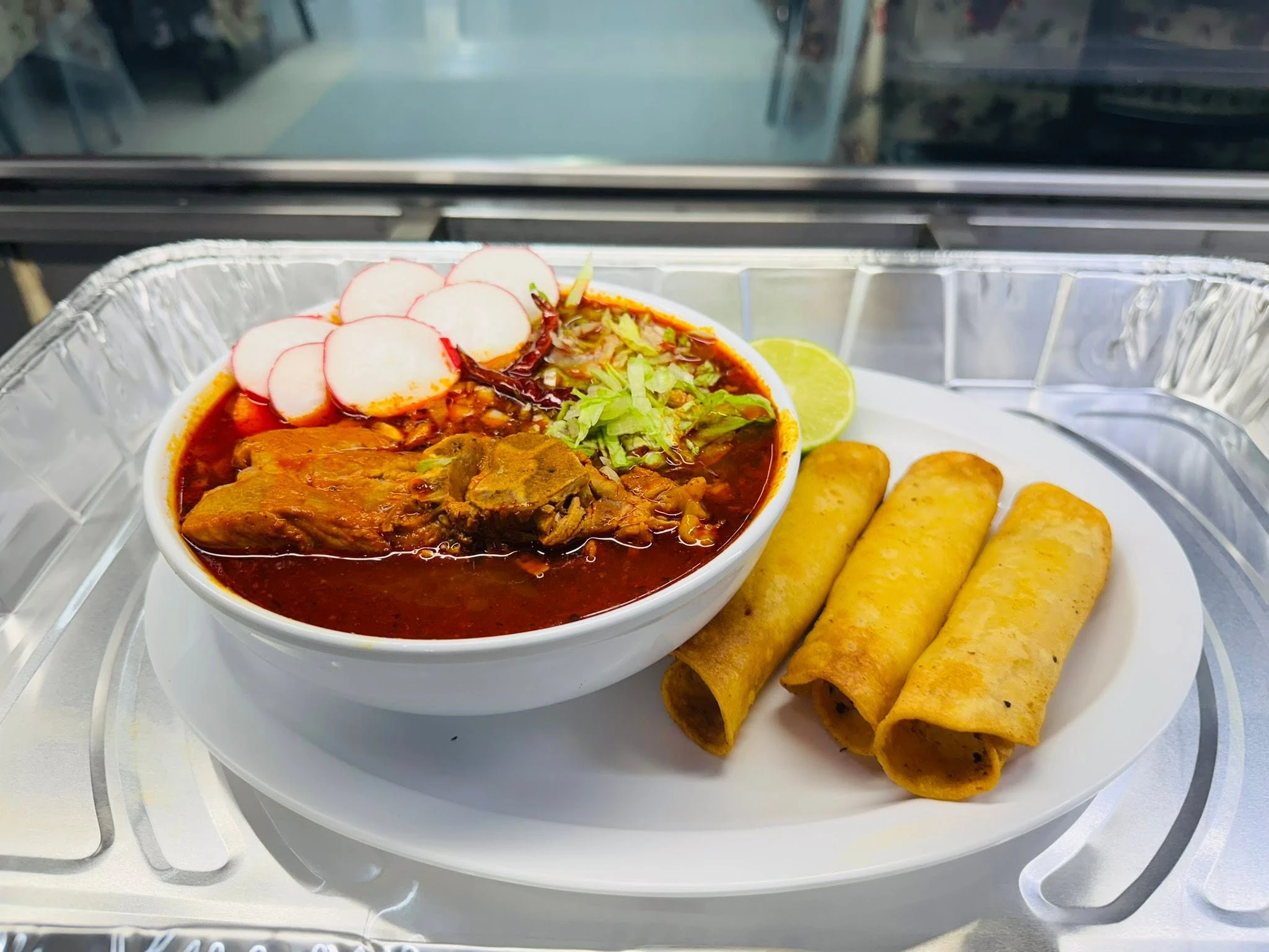 A fresh red broth soup plate served with rolled tacos at Carniceria Camargo