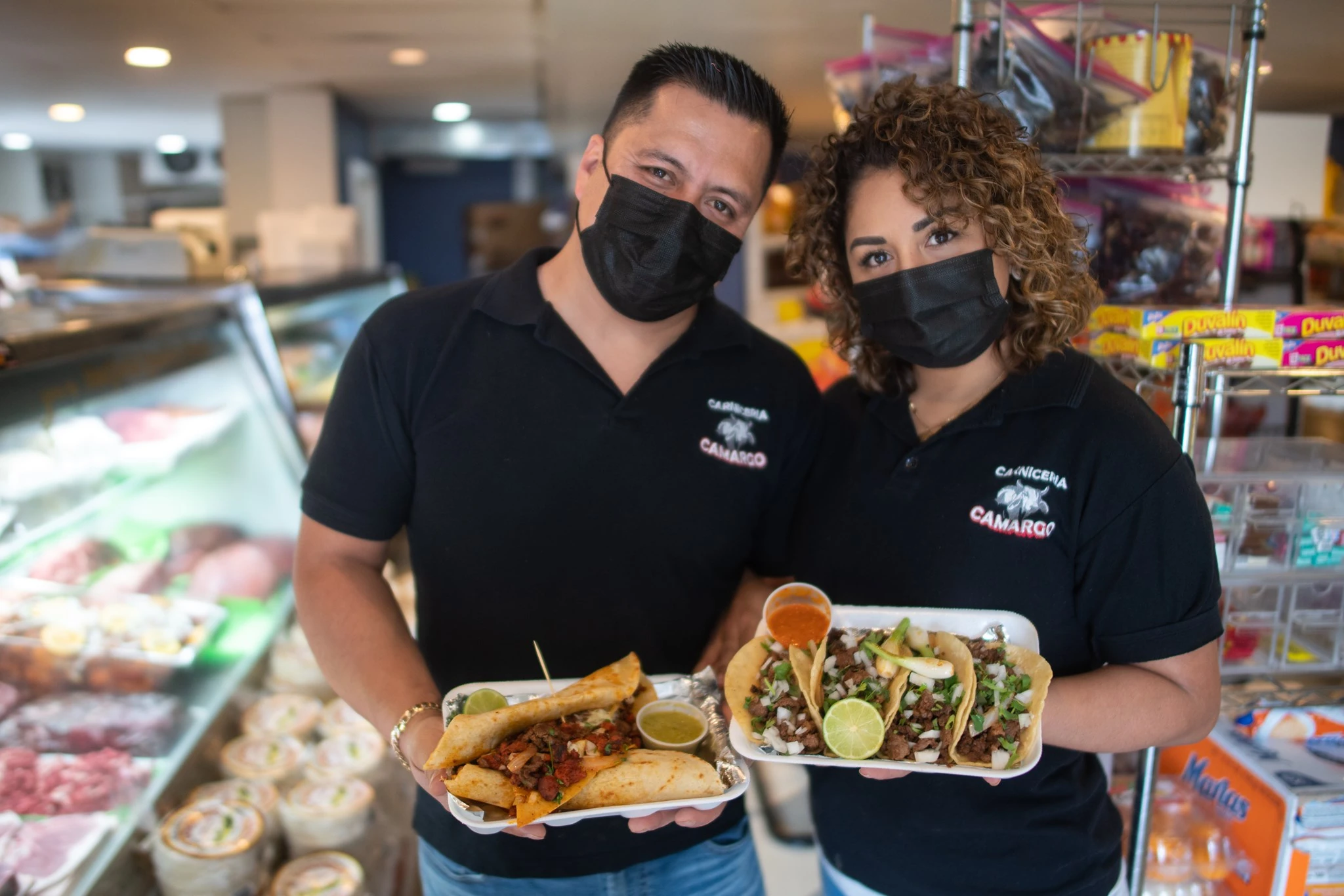 Two Carniceria Camargo team members inside the market holding taco plates for customers